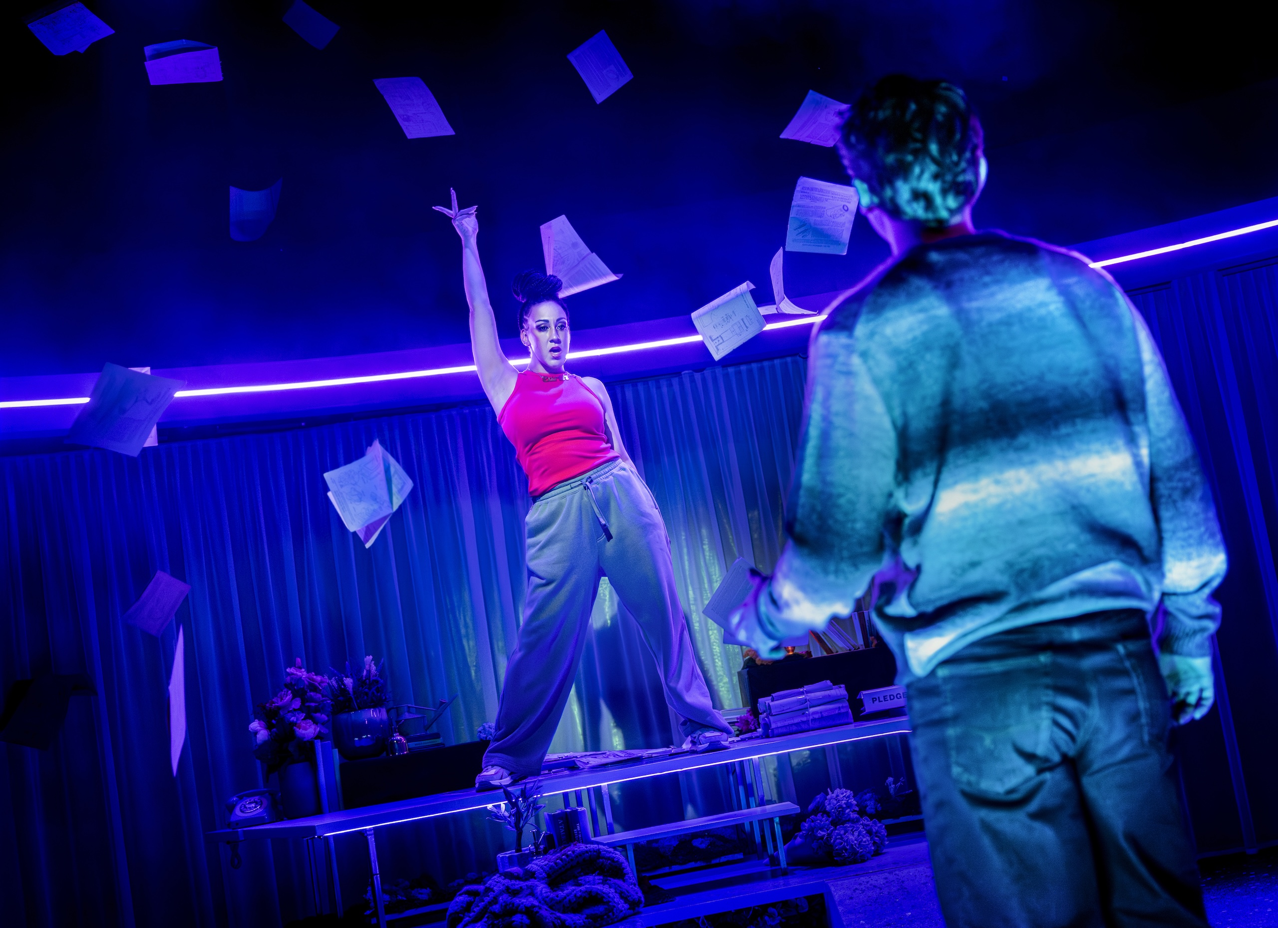 A stage set of a woman throw papers up in the air, viewed from behind a man.