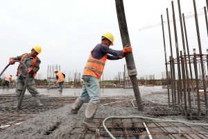 Construction workers pour concrete from a large hose onto a steel rebar grid at a building site