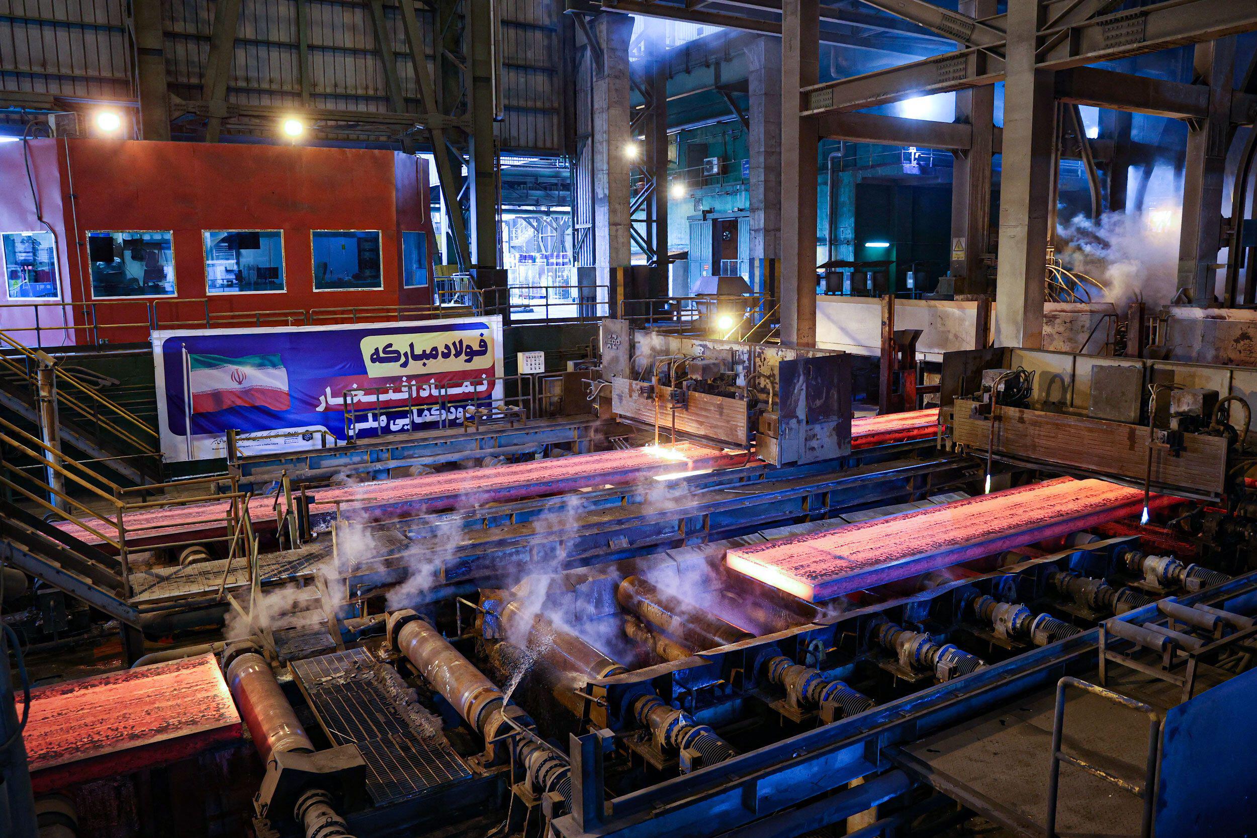 A steel mill interior showing glowing red-hot metal slabs moving along industrial rollers
