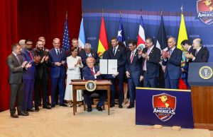 Un grupo de personas de pie y aplaudiendo alrededor de Donald Trump, quien está sentado