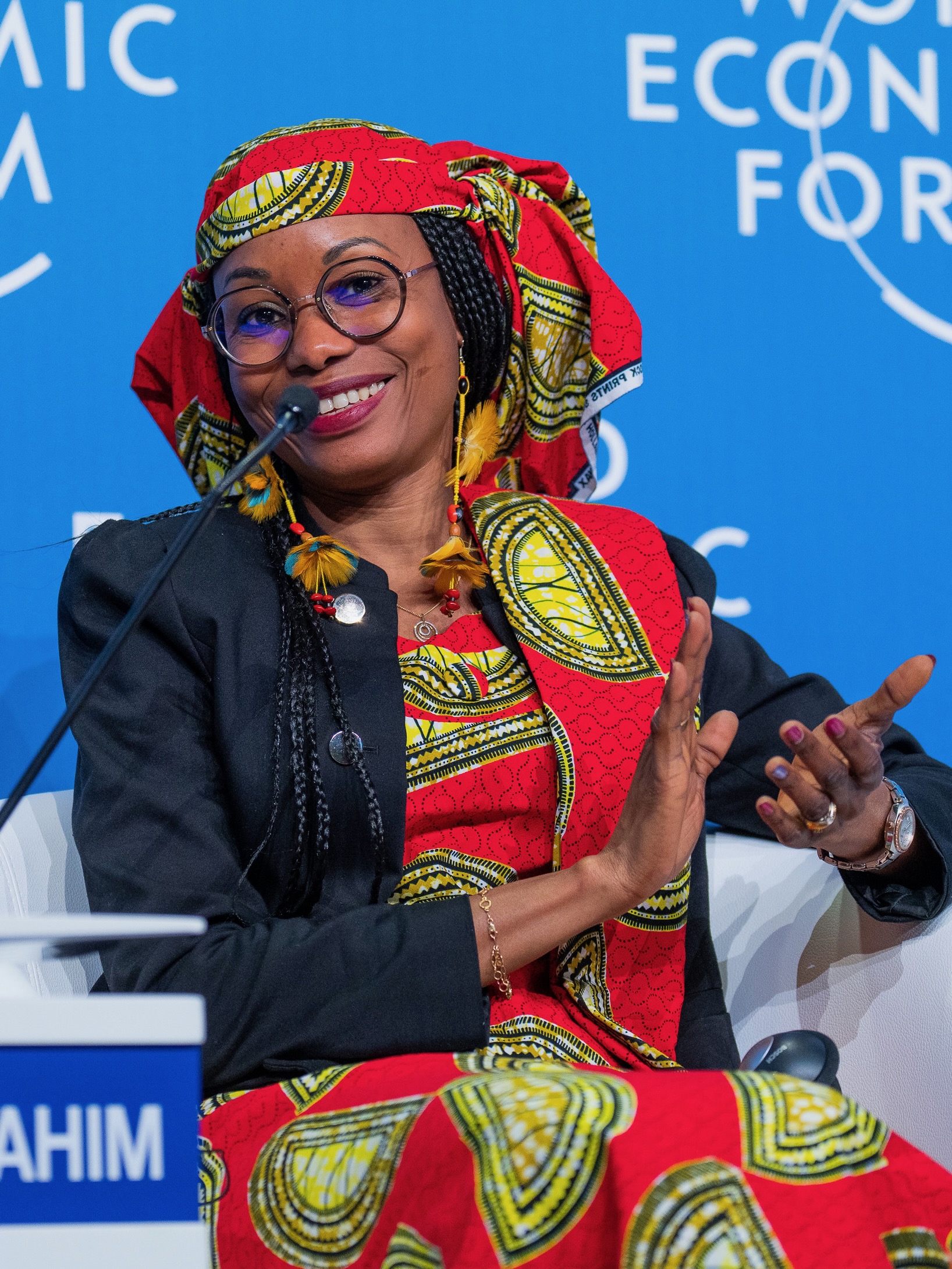 A woman wearing a vibrant red and yellow patterned headwrap a speaking at a World Economic Forum event.