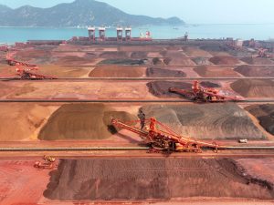 An aerial view of a large industrial port with massive piles of iron ore