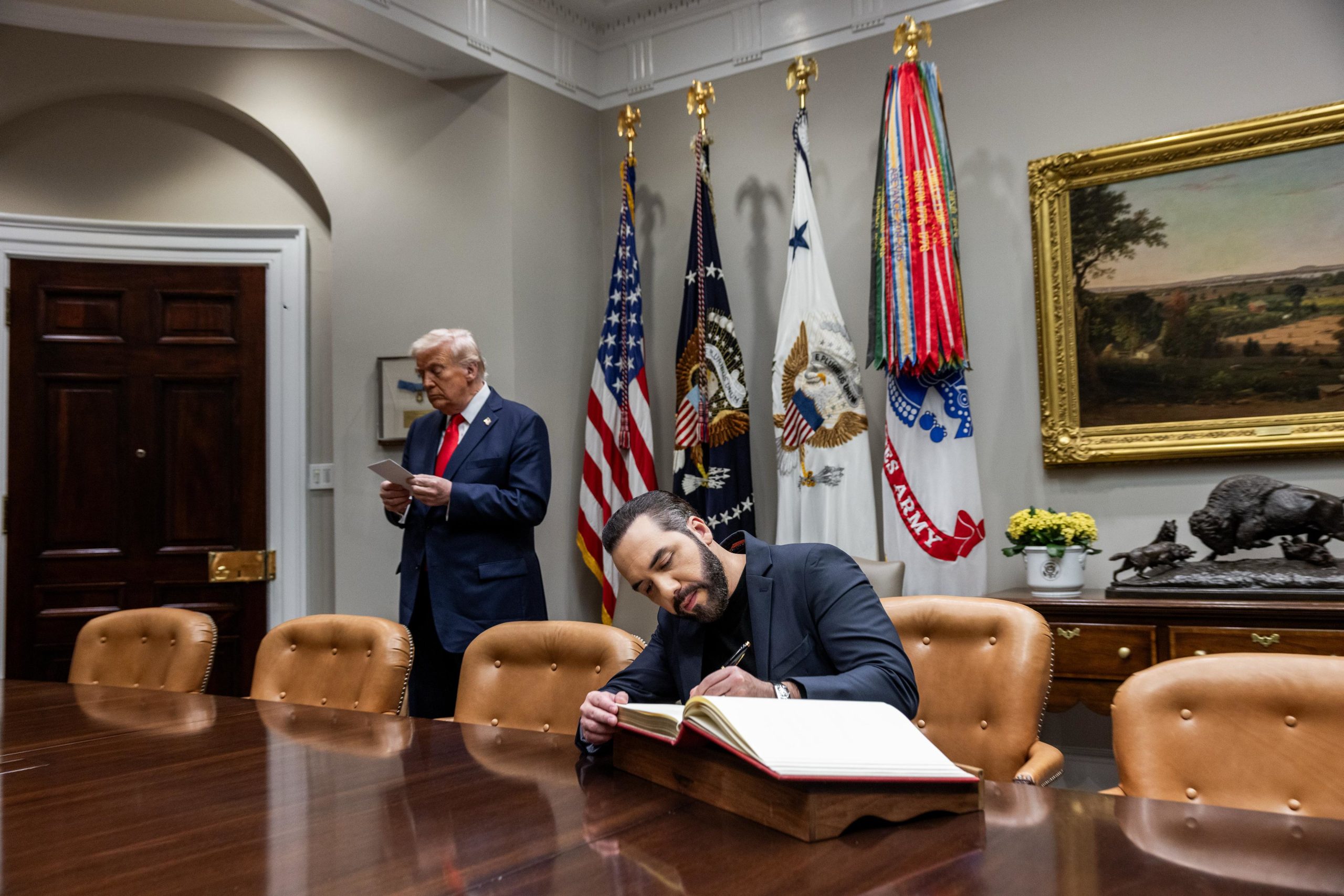 Donald Trump de pie junto a Nayib Bukele, quien está sentado