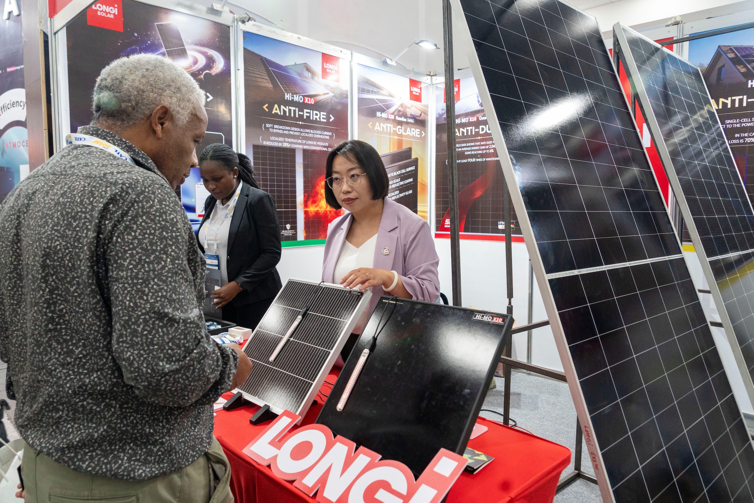 A saleswoman explains solar panel technology to a man at a trade show booth