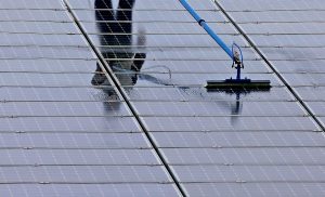 A worker uses a long pole with a brush attachment to clean solar panels