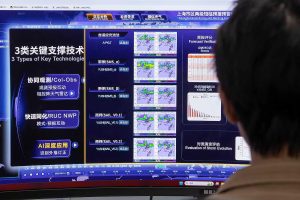 A person views a large computer screen displaying AI weather forecasting with various data charts, maps, and technical terminology.