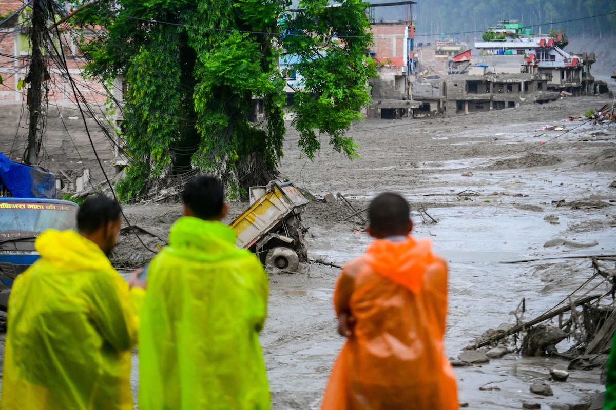 Three men in neon ponchos watched the aftermath of flash floods and mudslides