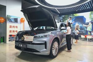A SUV with its front hood open is parked in a showroom while a woman stands beside it