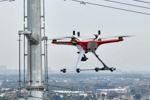 A red and white drone flying near power lines