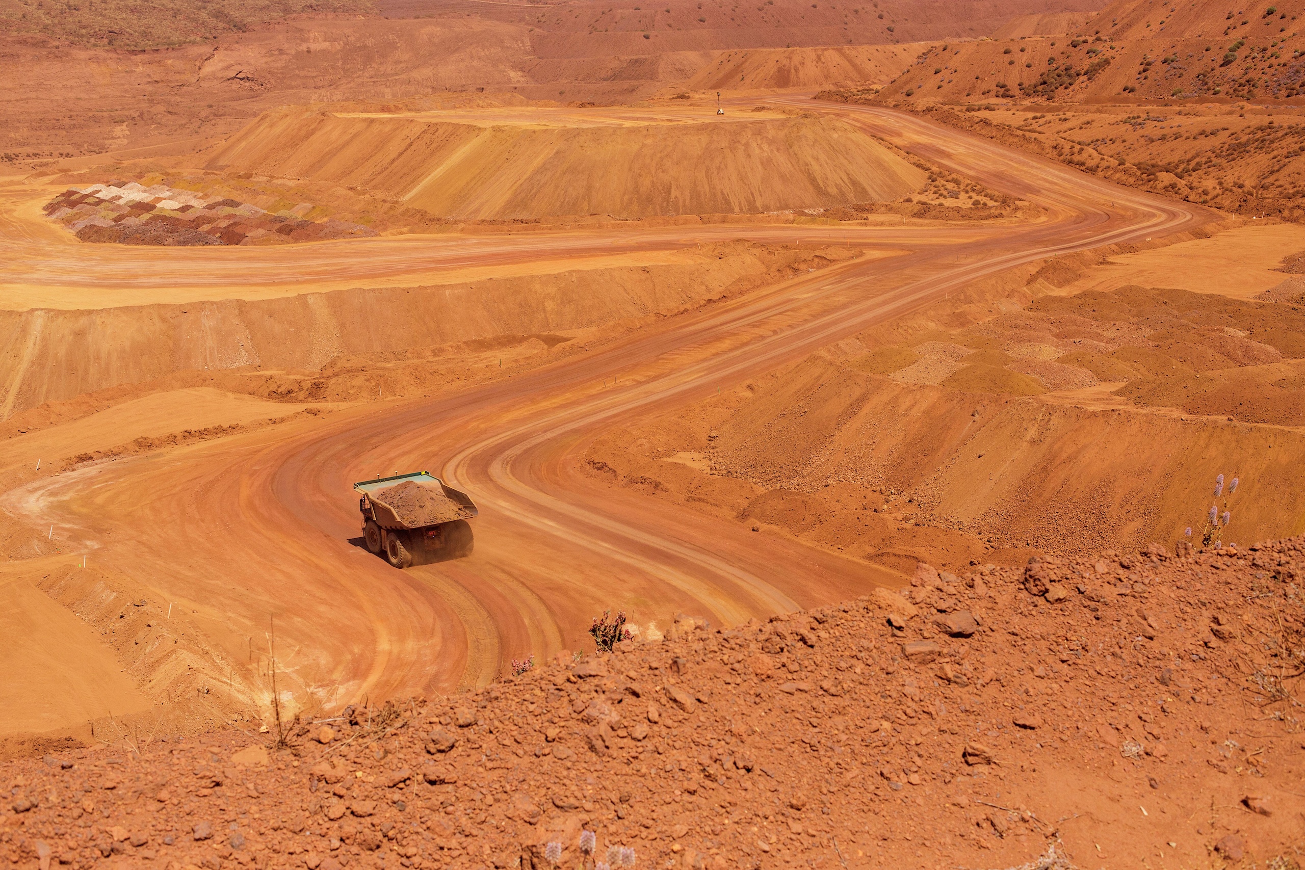 A large haul truck drives along a winding, unpaved road through a vast, open-pit mine