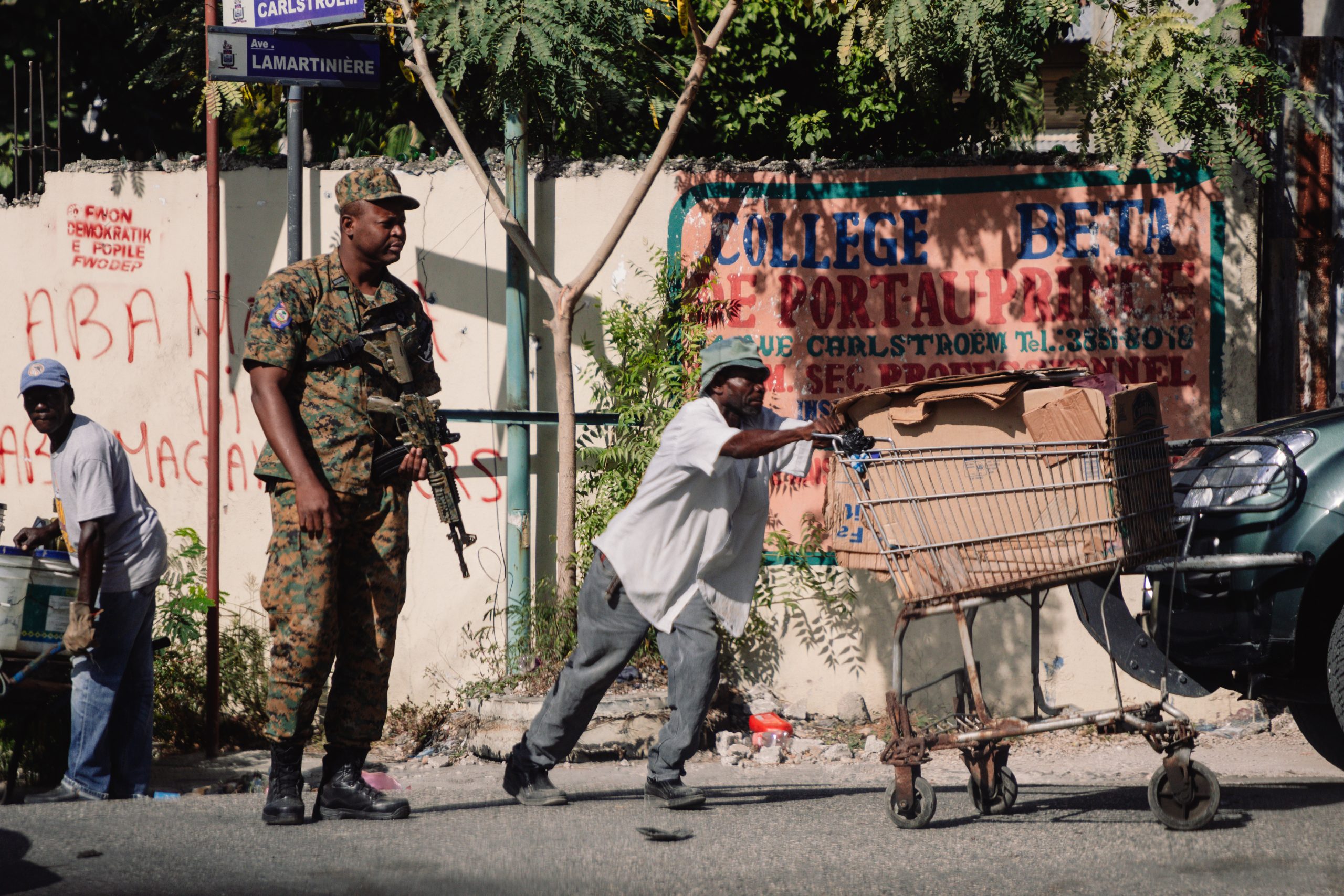 man pushes supermarket trolley near armed man wearing camouflage