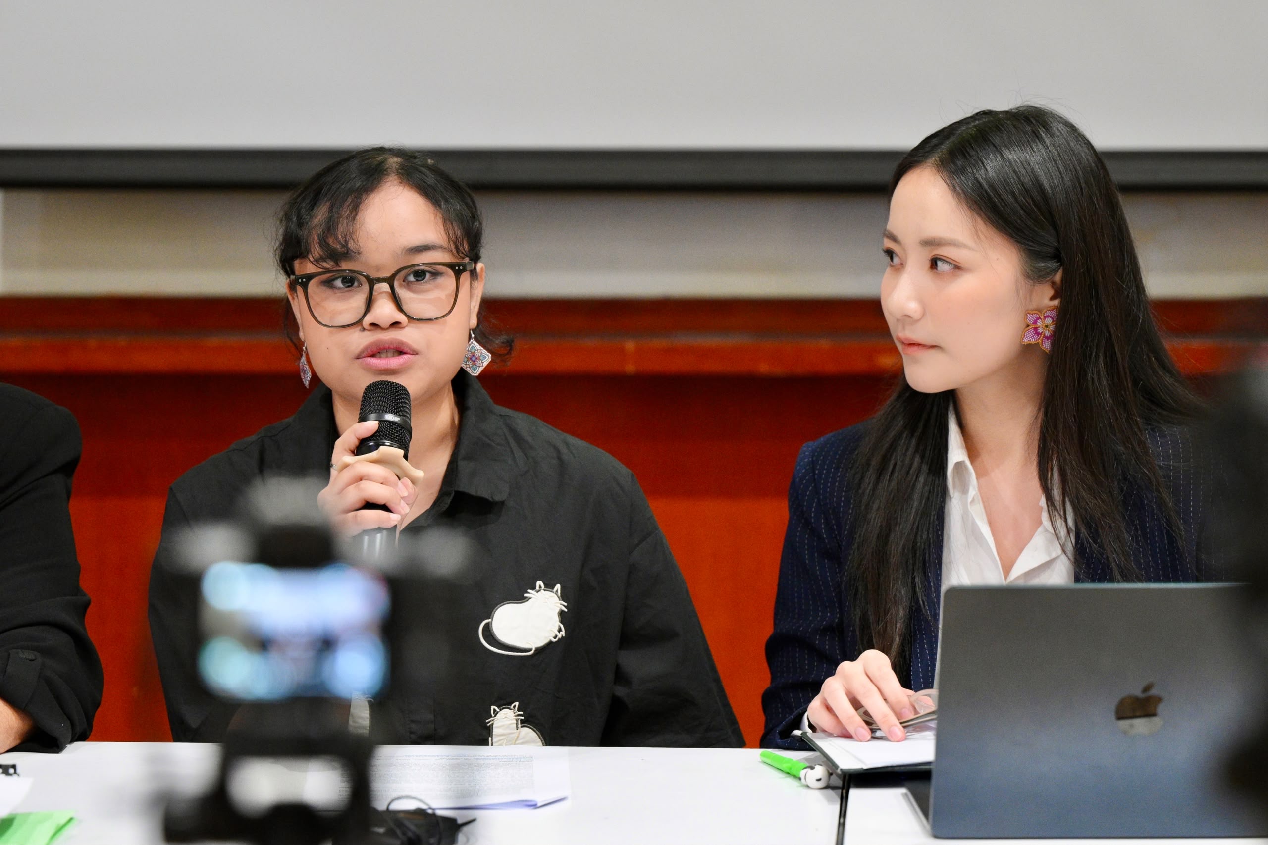 two seated women, one speaking into microphone
