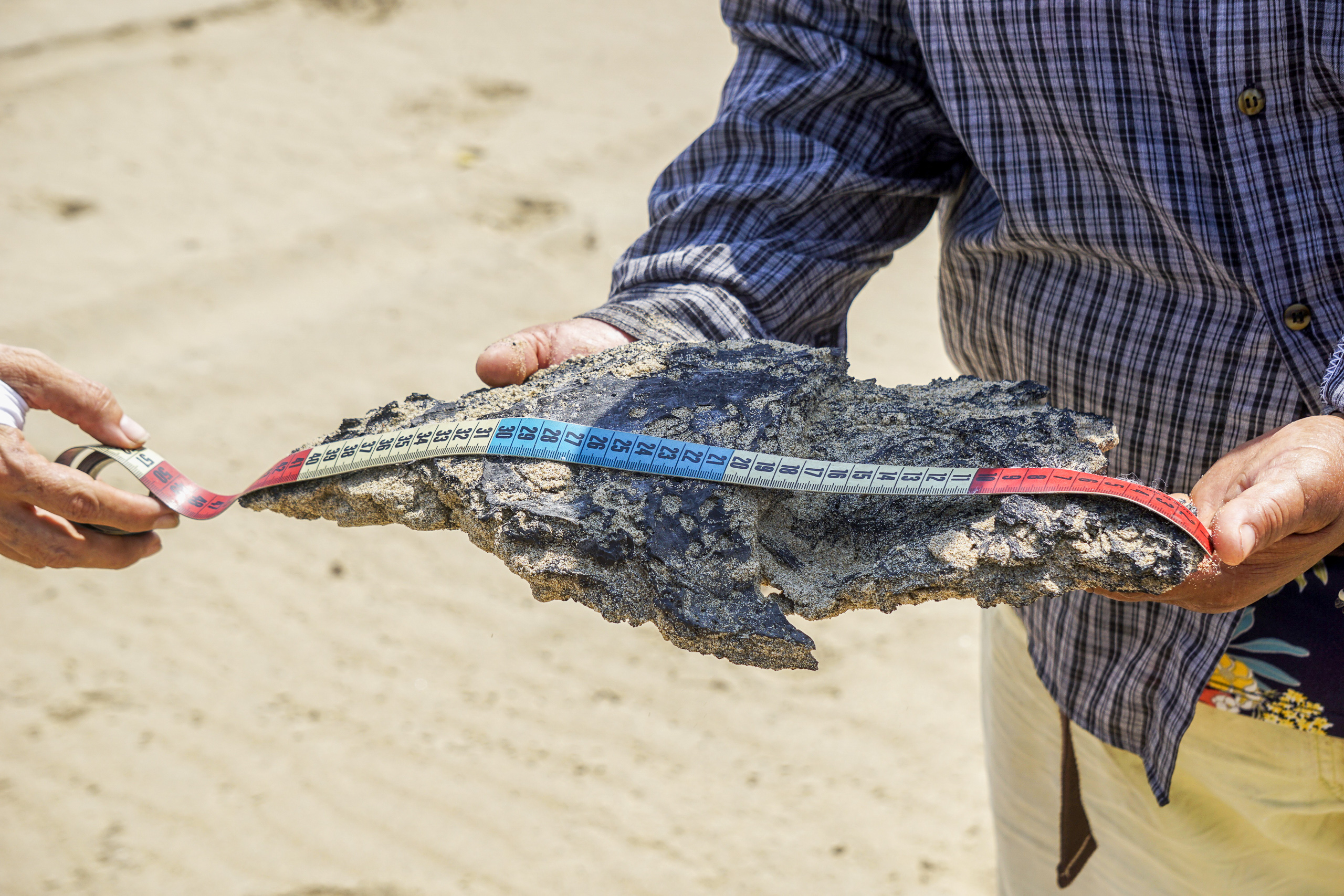 Los lugareños miden un trozo de chapopote en la playa de Agua Dulce