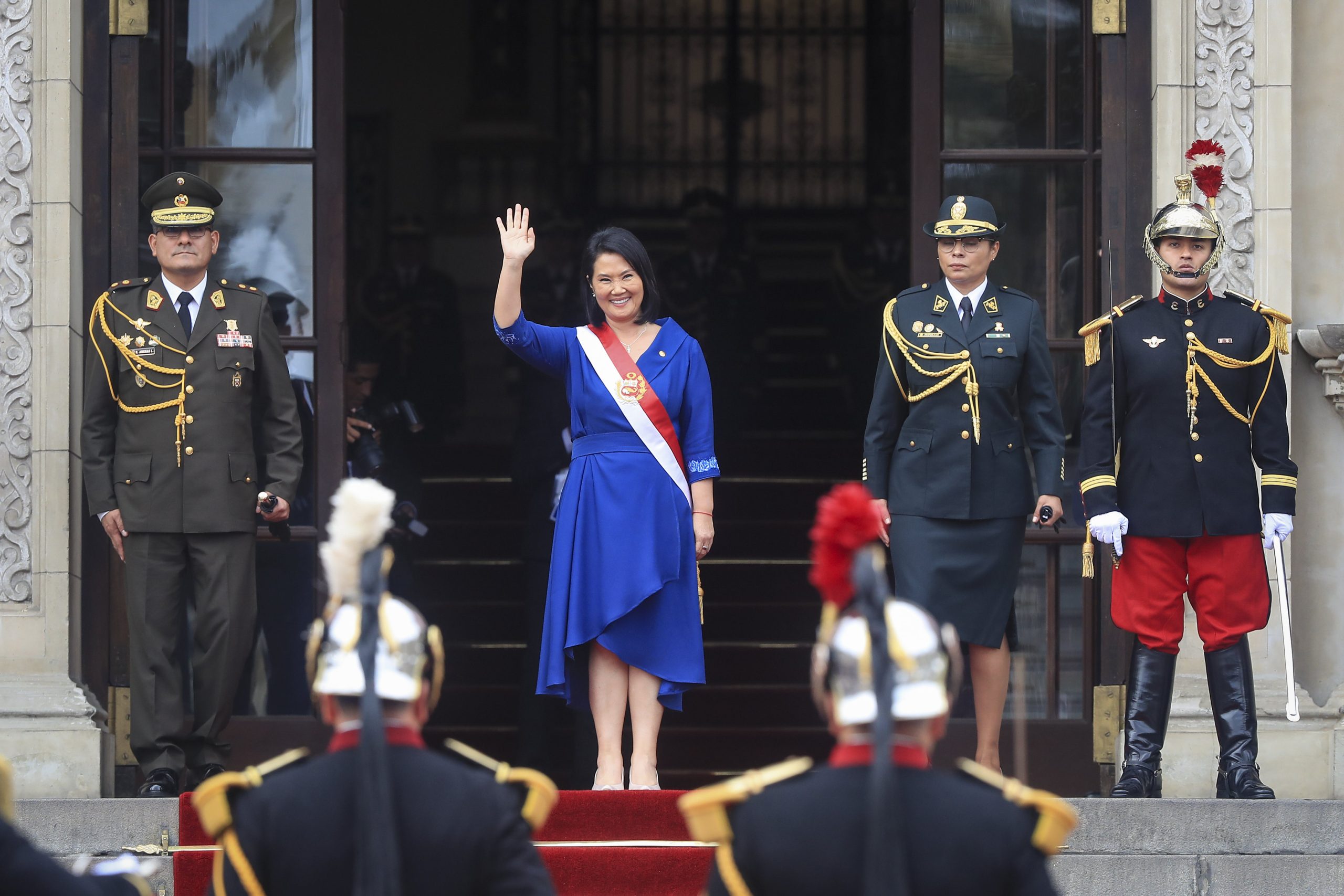 Keiko Fujimori waving while flanked by people in military uniforms
