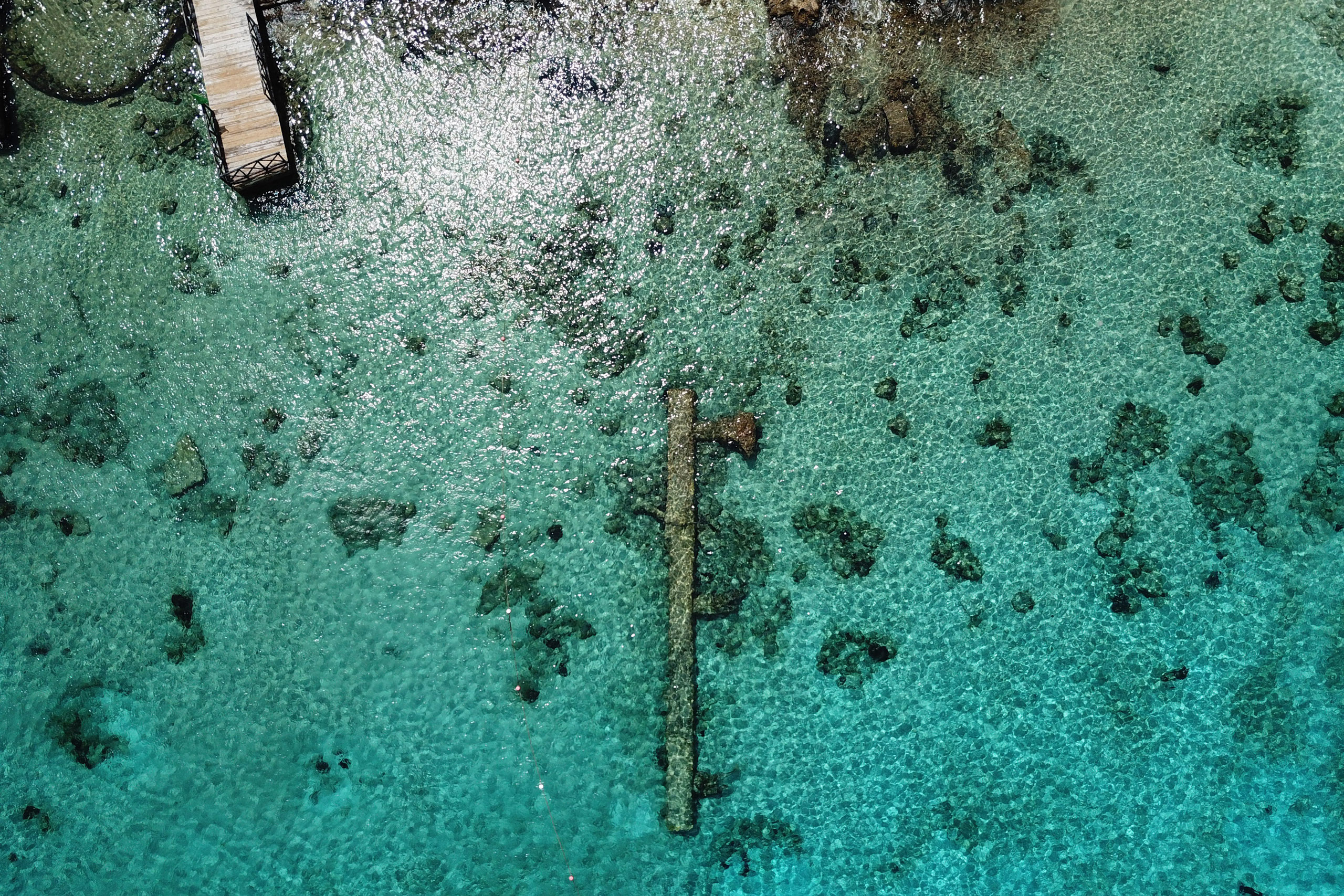 Aerial shot of turquoise coastal water with rocks on the seafloor