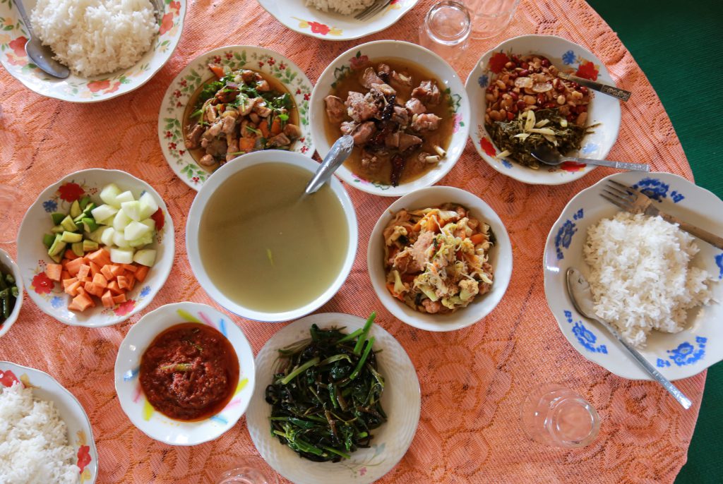 A traditional Myanmar meal showing soup, various side dishes, raw vegetables
